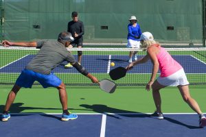 two couples play pickleball on a bright green and blue court