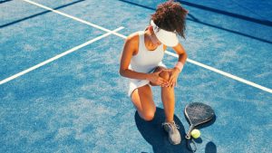 woman on pickleball court holding her knee in pain